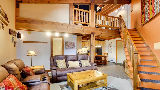 A spacious living area with a brown leather sofa, a wooden coffee table, and a staircase leading to an upper level. - Silverthorne Condo W/pool Access - Shuttle to Town (Silverthorne)
