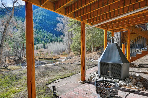 A covered outdoor area with a fireplace, wooden beams, and a view of a forested mountain.
