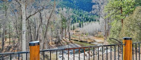 A wooden fence with metal railings overlooking a mountainous landscape with a stream and trees.