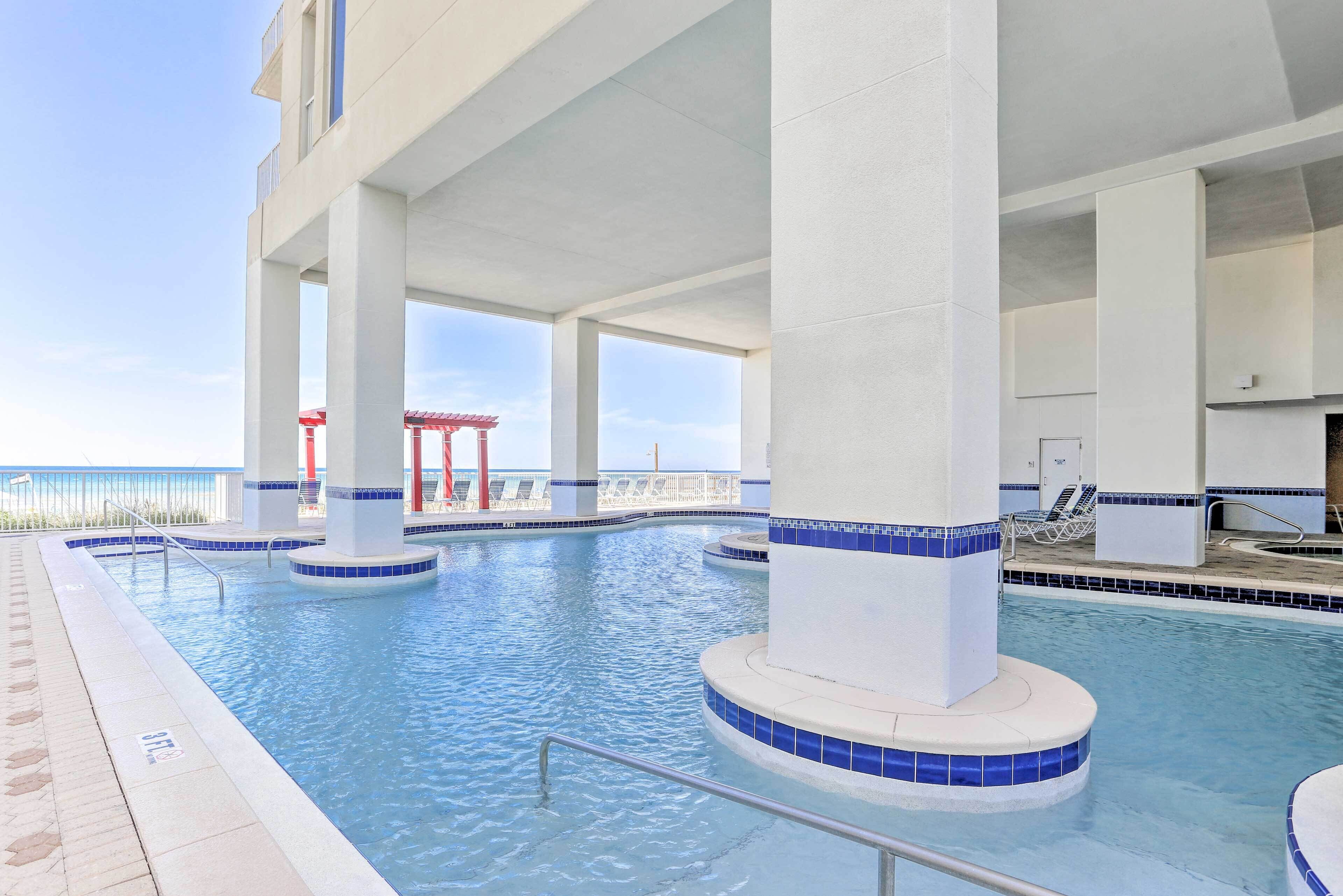 An indoor swimming pool with clear blue water, white columns, and a view of the ocean.