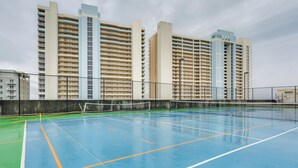 Un court de tennis intérieur, doté d’un filet et entouré d’une clôture, avec des immeubles de grande hauteur en arrière-plan.