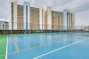Un campo da tennis al coperto con rete, circondato da una recinzione, con grattacieli sullo sfondo.