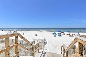 Una terraza de madera que da a una playa de arena blanca, sombrillas azules y sillas de playa.
