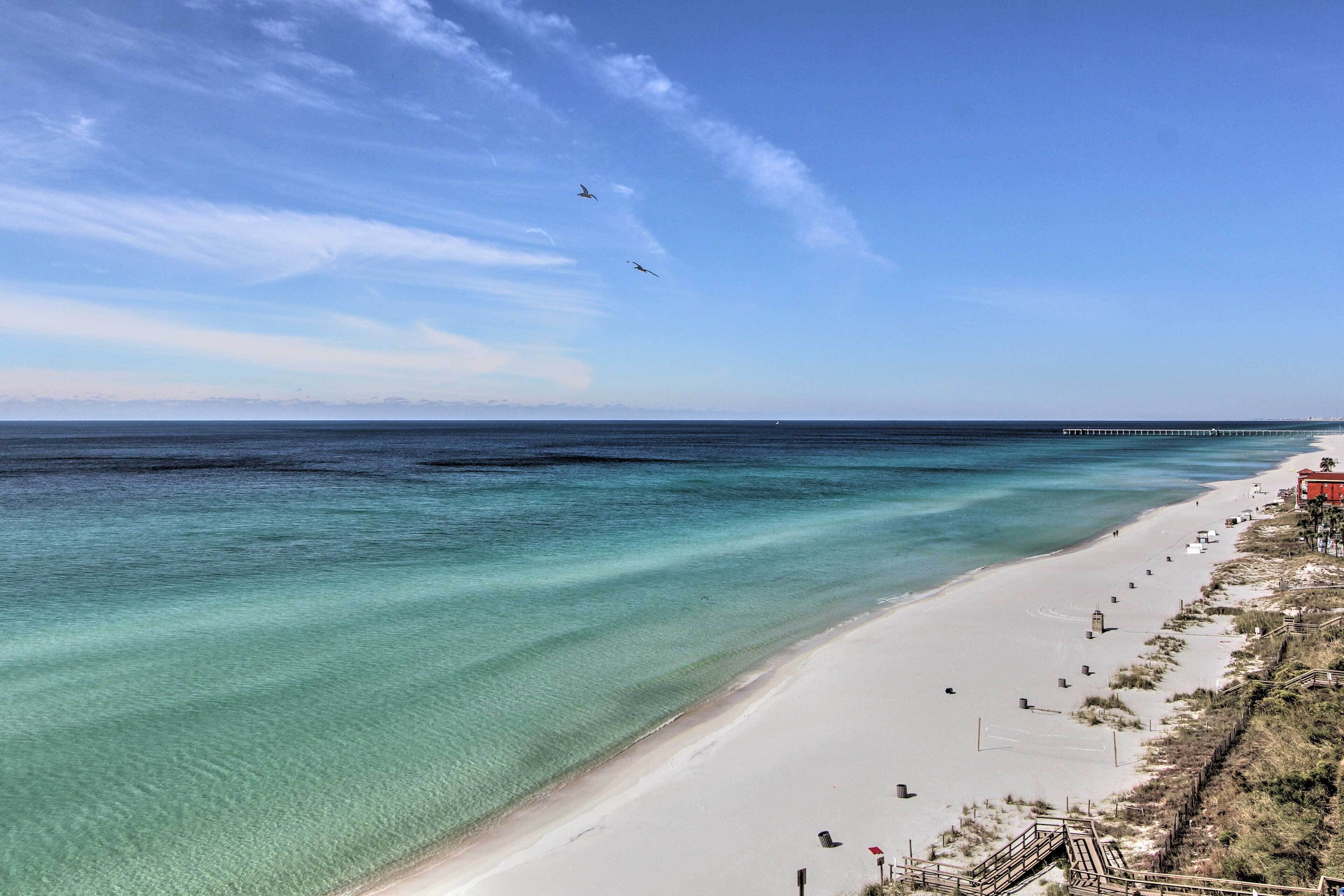 Ein Strand mit klarem türkisblauem Wasser, einem Sandufer und einem Steg, der sich ins Meer erstreckt.
