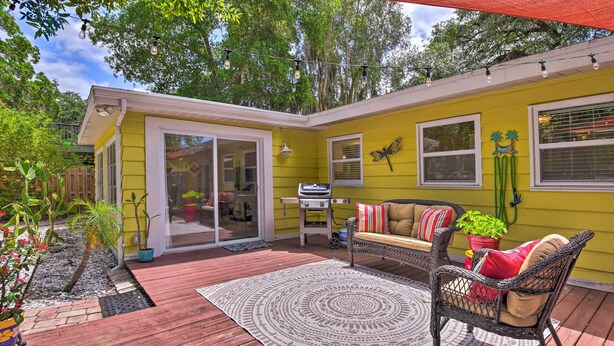 Une maison jaune avec une terrasse en bois, un canapé en osier et un barbecue.