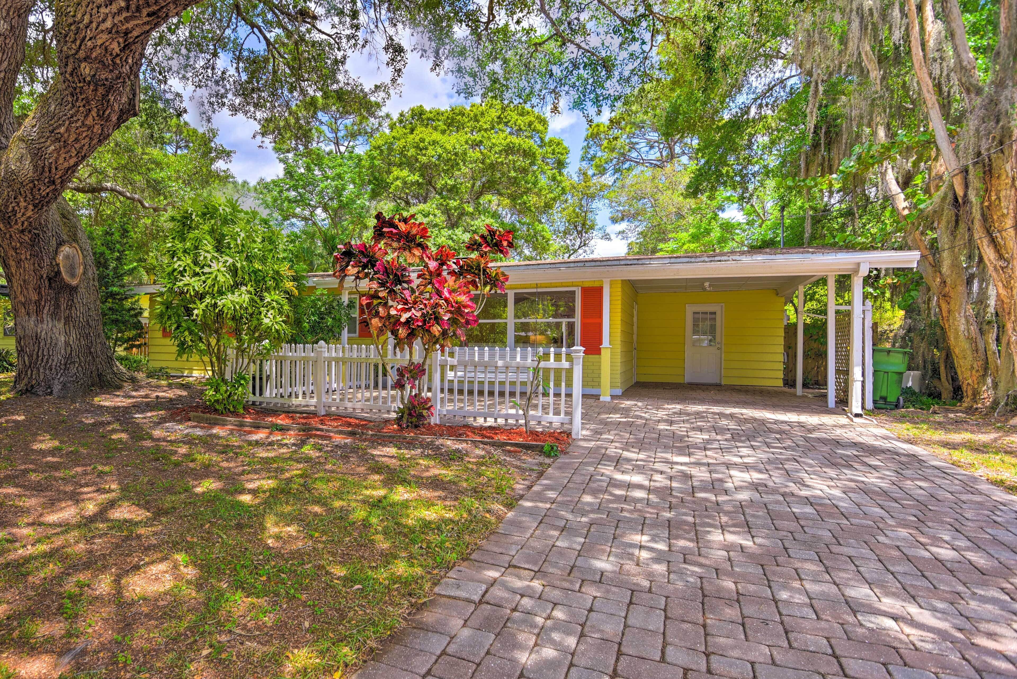 A yellow house with a brick pathway leading to a white picket fence and a porch.