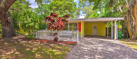 A yellow house with a brick pathway leading to a white picket fence and a porch.