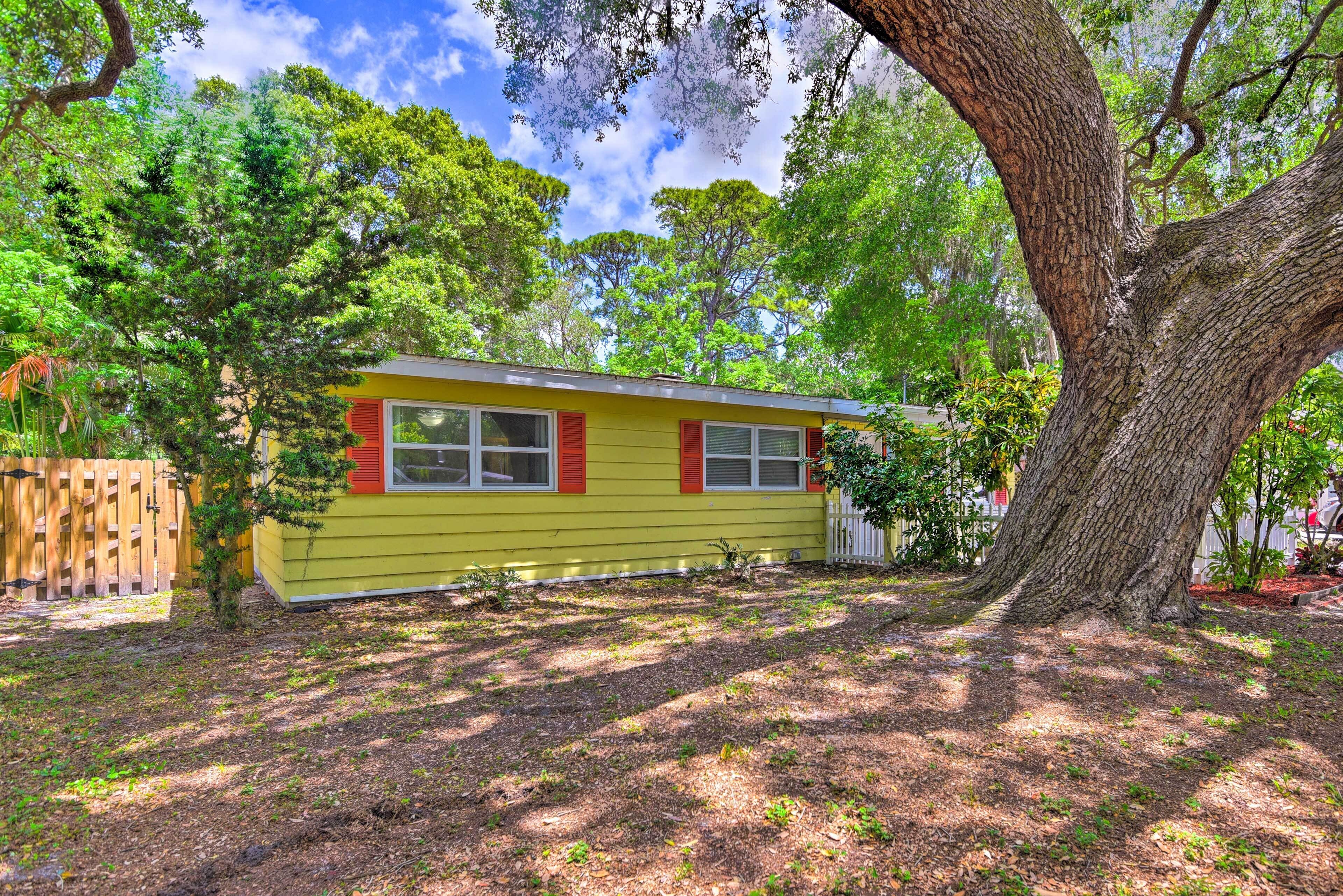 A yellow house with red shutters, surrounded by trees and a wooden fence.