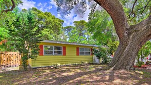 Une maison jaune aux volets rouges, entourée d’arbres et d’une clôture en bois.