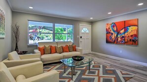 Un salon comprenant un canapé, des fauteuils, une table basse en verre et un tapis à motifs.