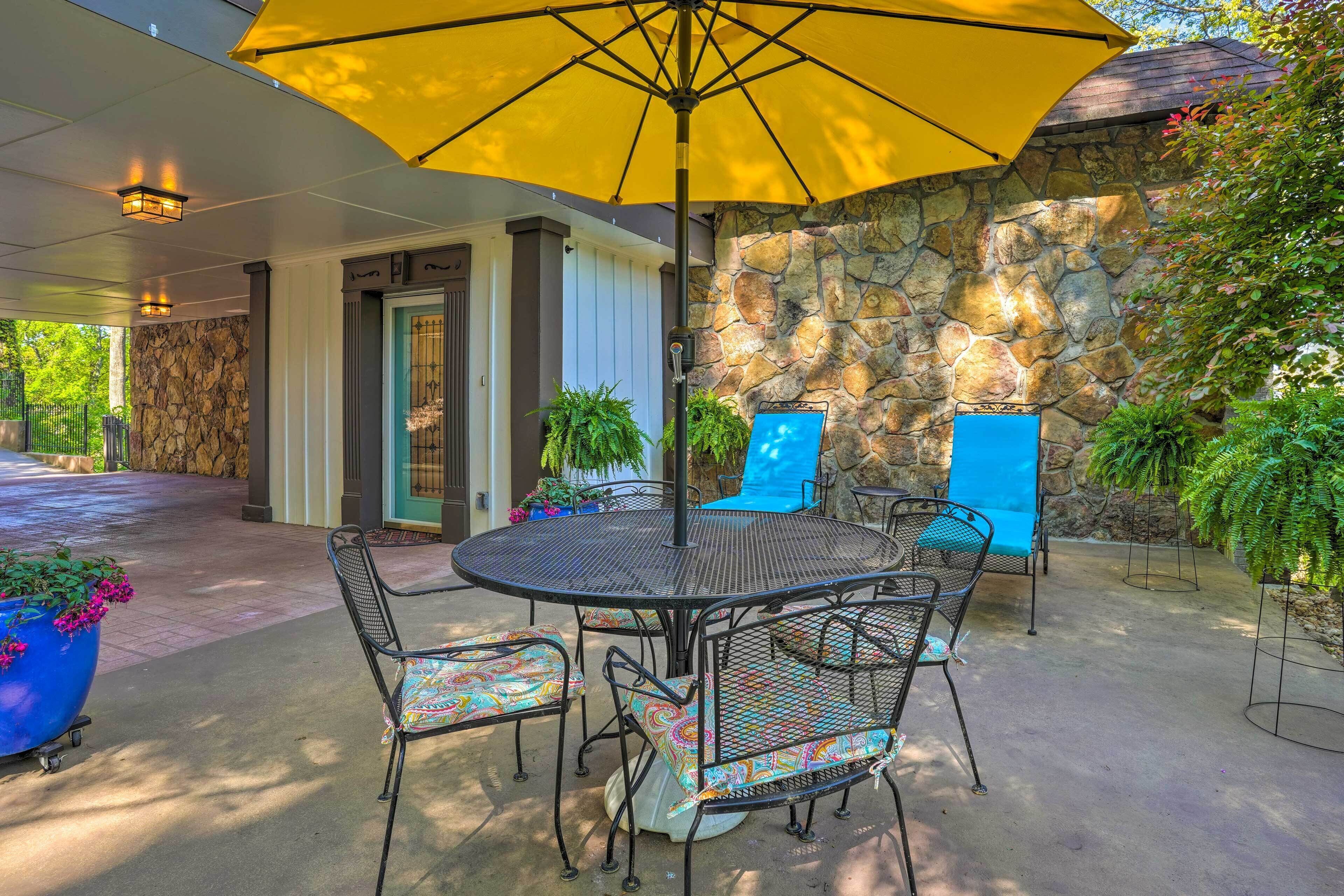A covered patio area with a round metal table and chairs, a yellow umbrella, and stone walls.