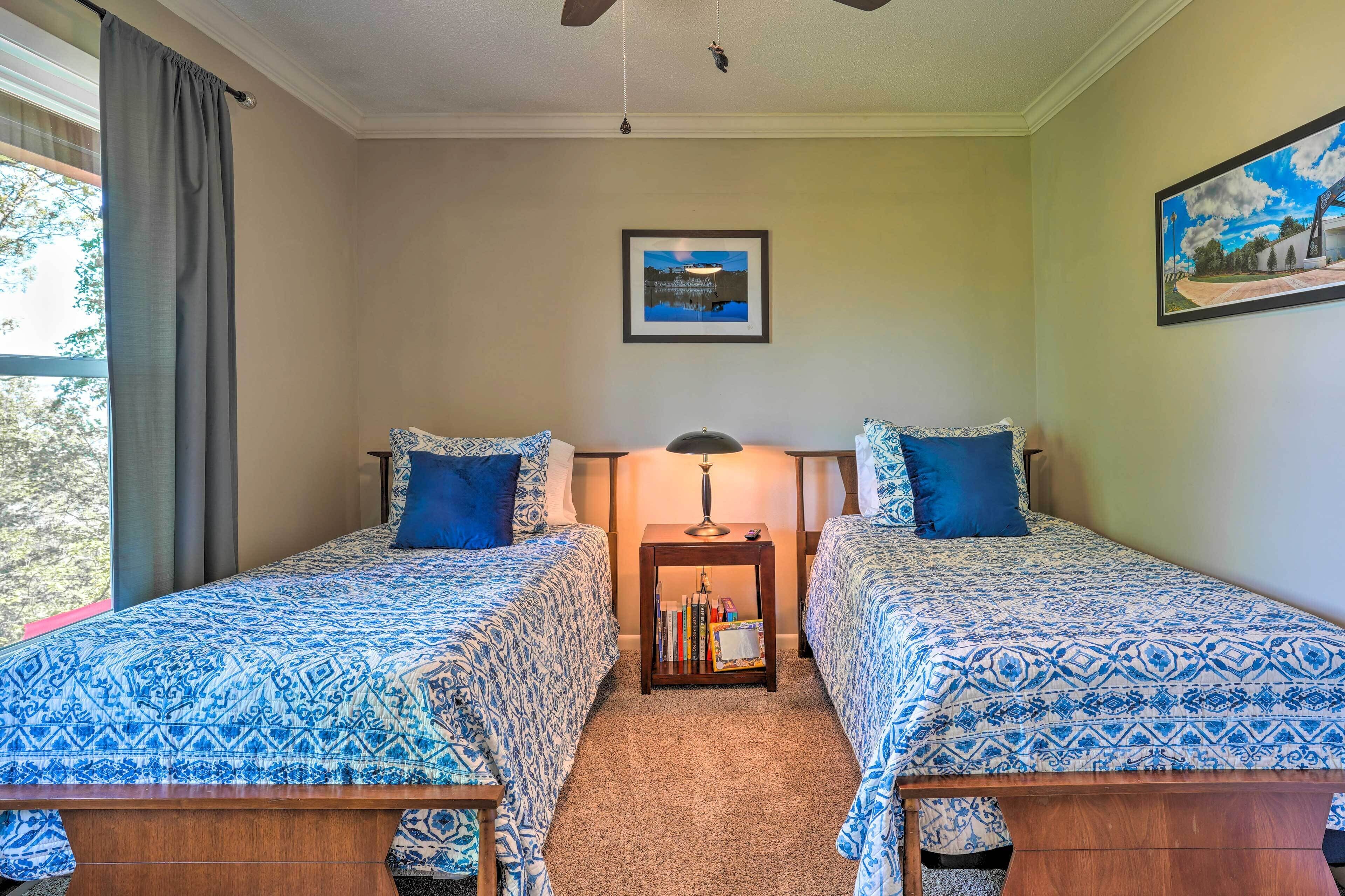 A room with two beds, a nightstand, a lamp, and a framed picture on the wall.