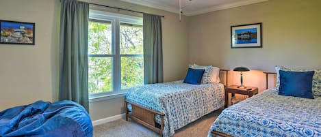 Un dormitorio con dos camas, ventilador de techo, sillón de saco y ventana con cortinas.