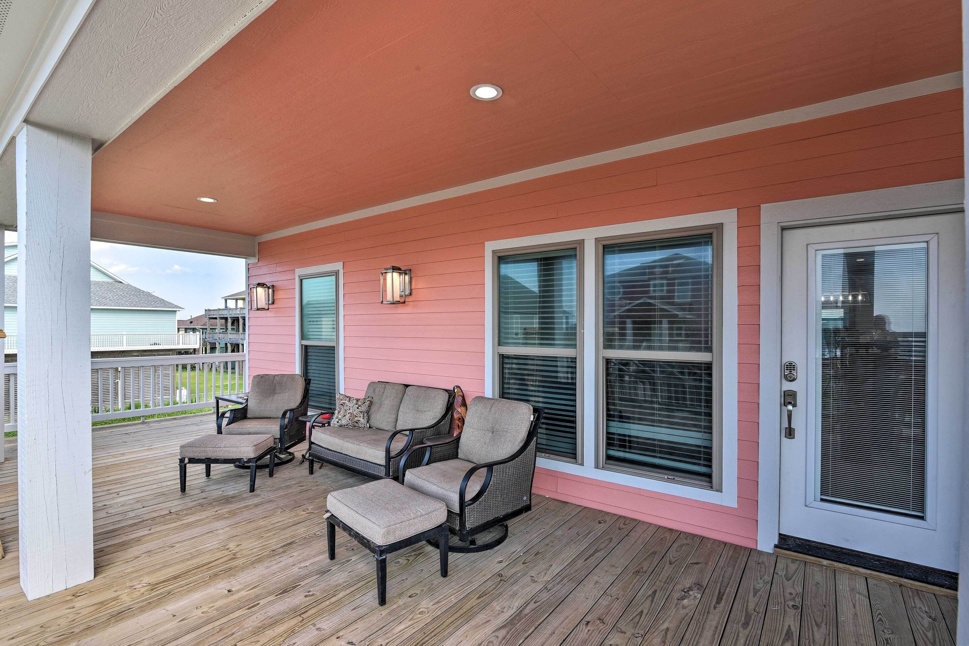 A covered porch with a pink exterior, two chairs, a table, and a bench.