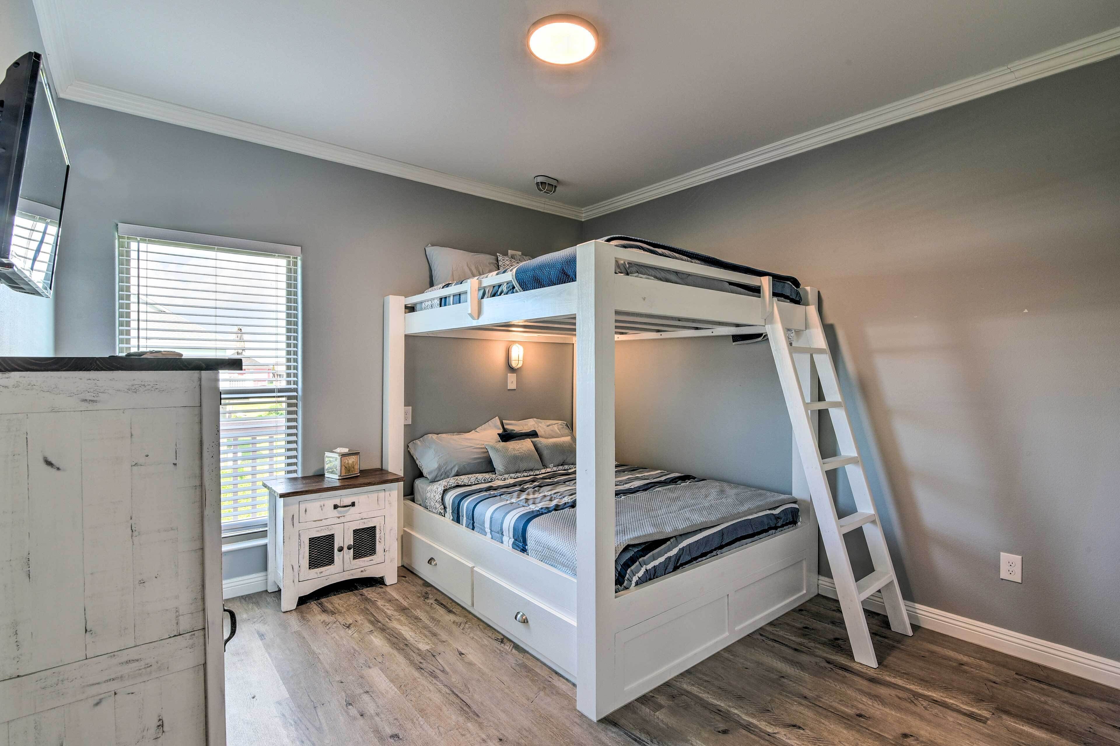 A bunk bed with a ladder, a bedside table, and a window with blinds.