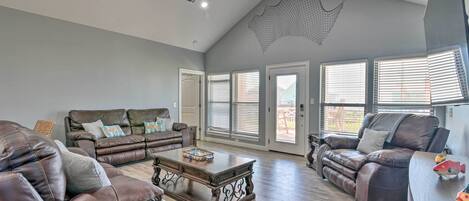 A spacious living room with a ceiling fan, large windows with blinds, and a fireplace.