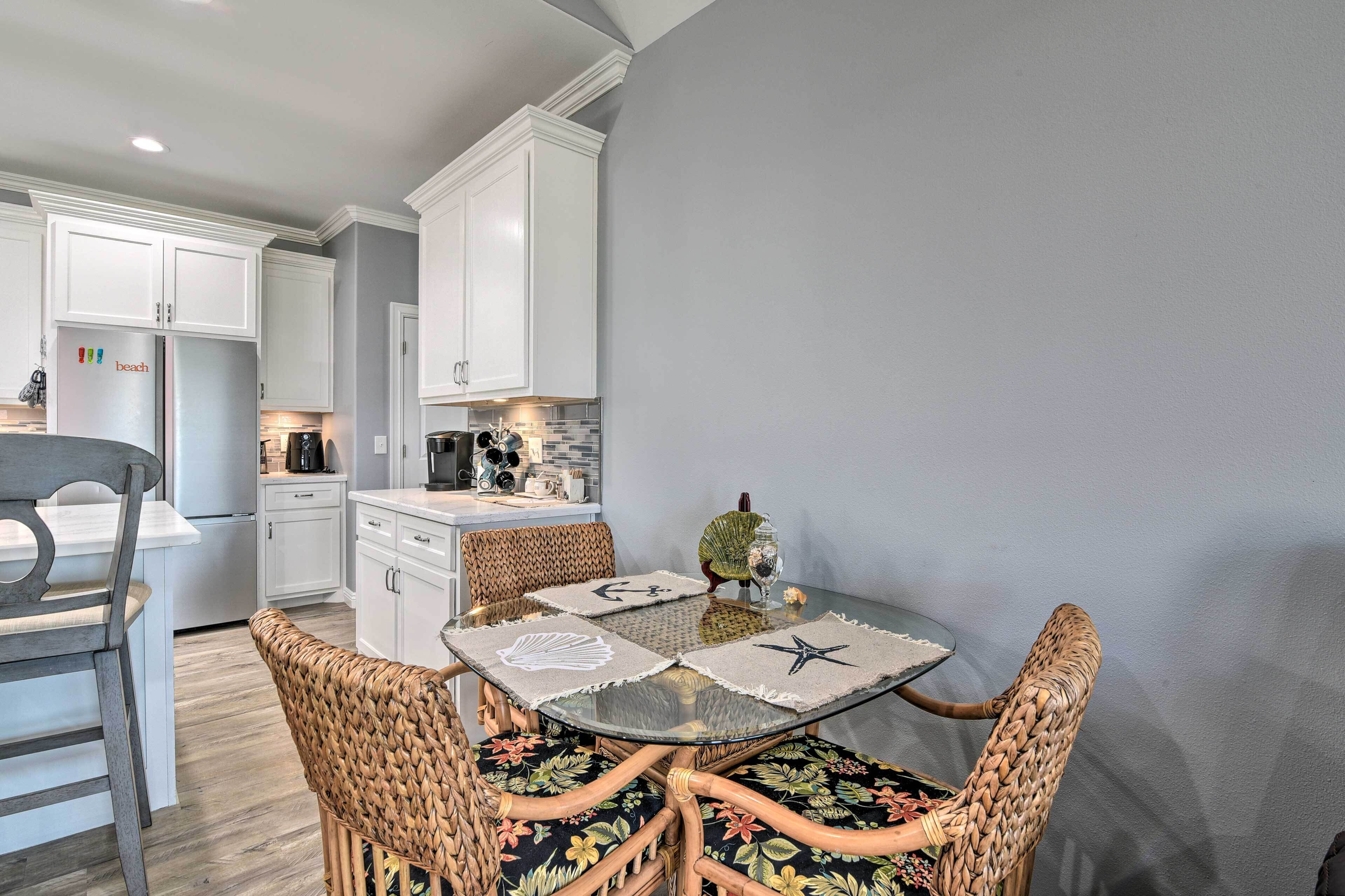 Una cocina moderna con armarios blancos, una mesa de comedor con sillas tejidas y una pequeña isla con una cafetera.