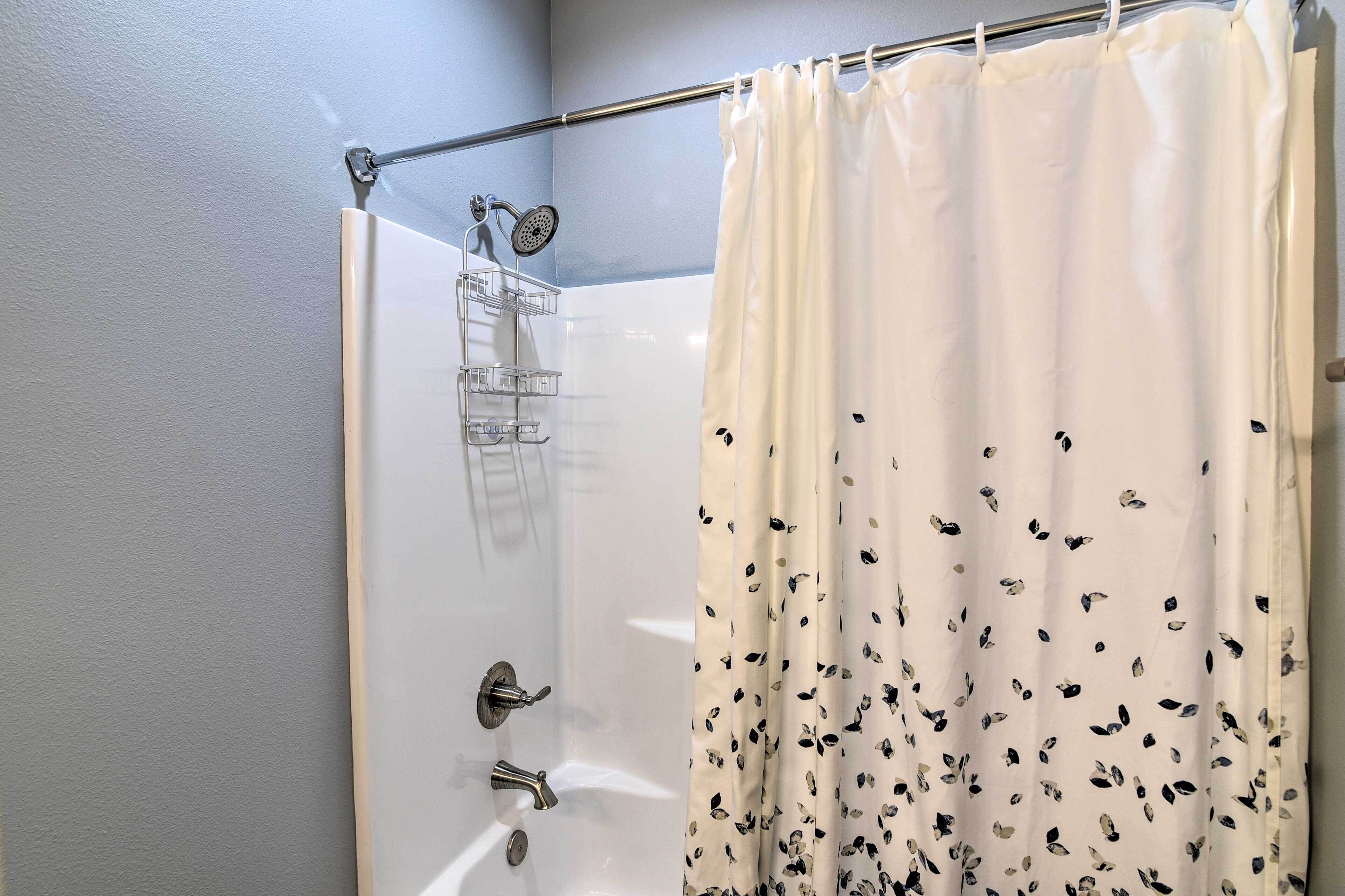 Ducha con cortina blanca adornada con hojas, ducha de mano y grifo empotrado en la pared.