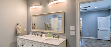 A bathroom with a white vanity, two sinks, a large mirror, and a shower curtain.