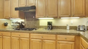 A kitchen with wooden cabinets, granite countertops, a stove, a coffee maker, and a toaster. - Indio Home W/private Pool & Putting Green By Golf (Indio)