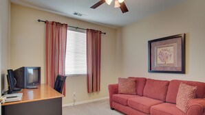 A room with a wooden desk, a red couch, a ceiling fan, and a framed picture on the wall. - Indio Home W/private Pool & Putting Green By Golf (Indio)