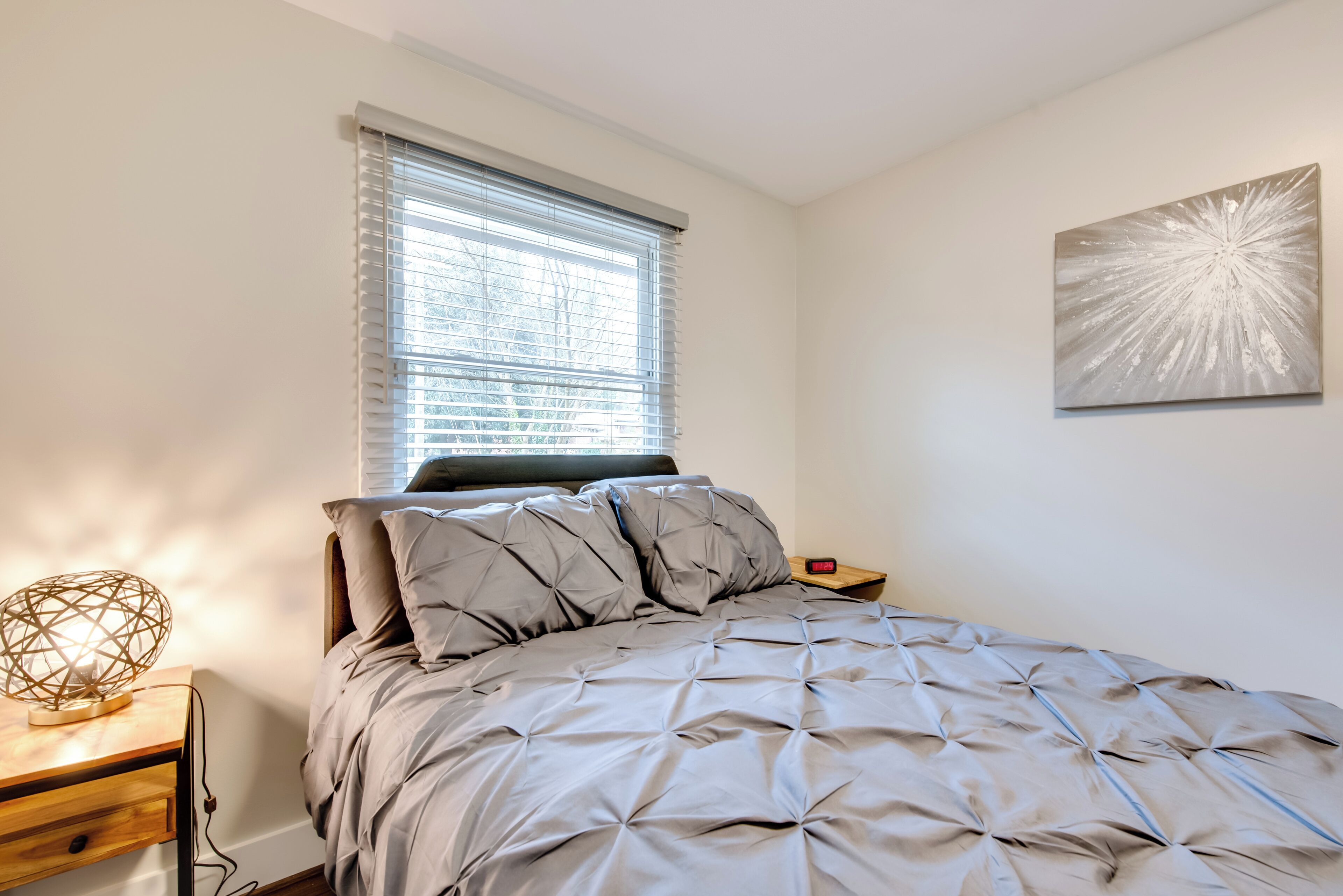 A bedroom with a bed, a nightstand, a lamp, and a window with blinds.