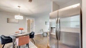 A modern kitchen with a stainless steel refrigerator, a dining table with chairs, and a pendant light.
