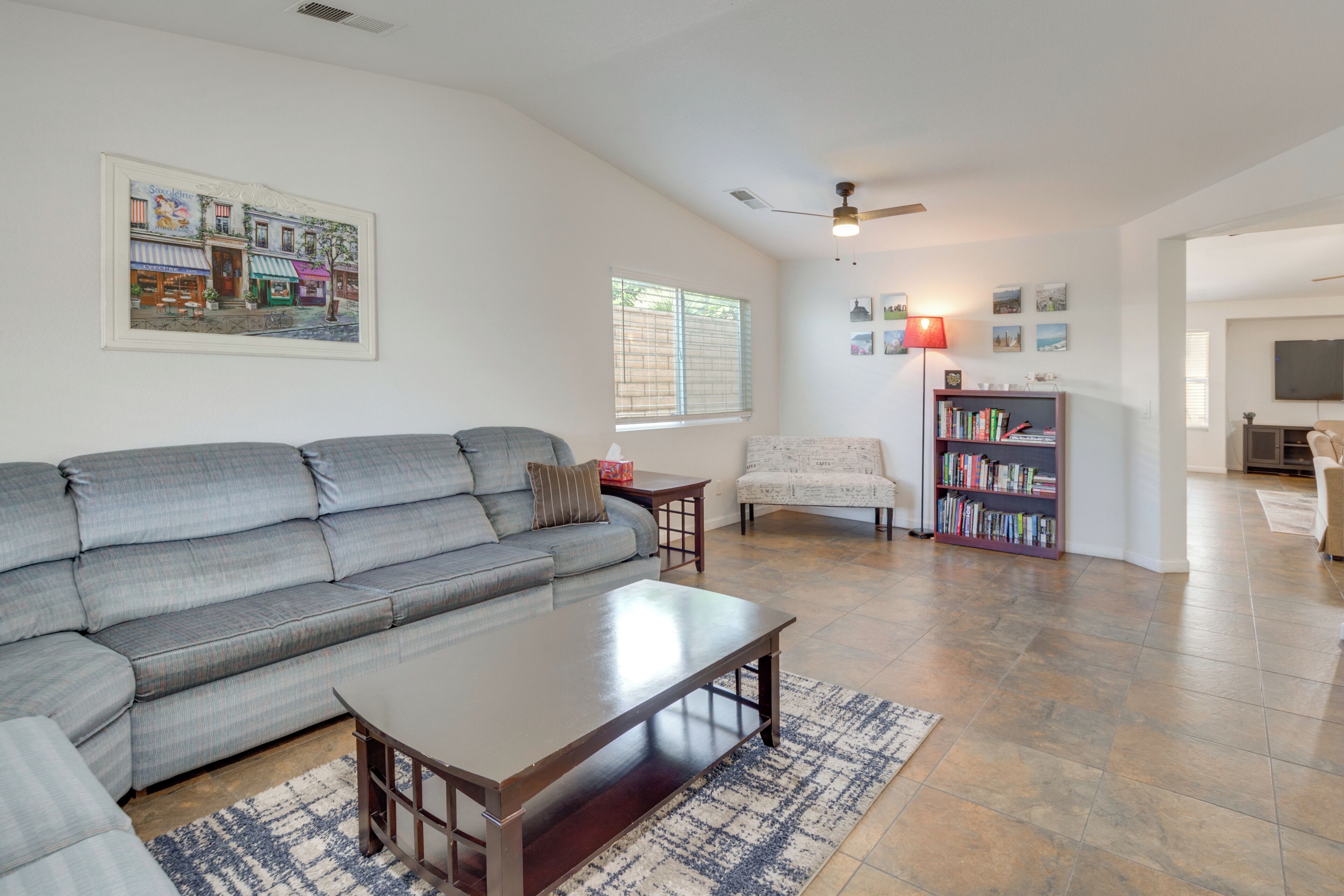 A living room with a gray sectional sofa, a wooden coffee table, a patterned rug, a bookshelf, and a ceiling fan.