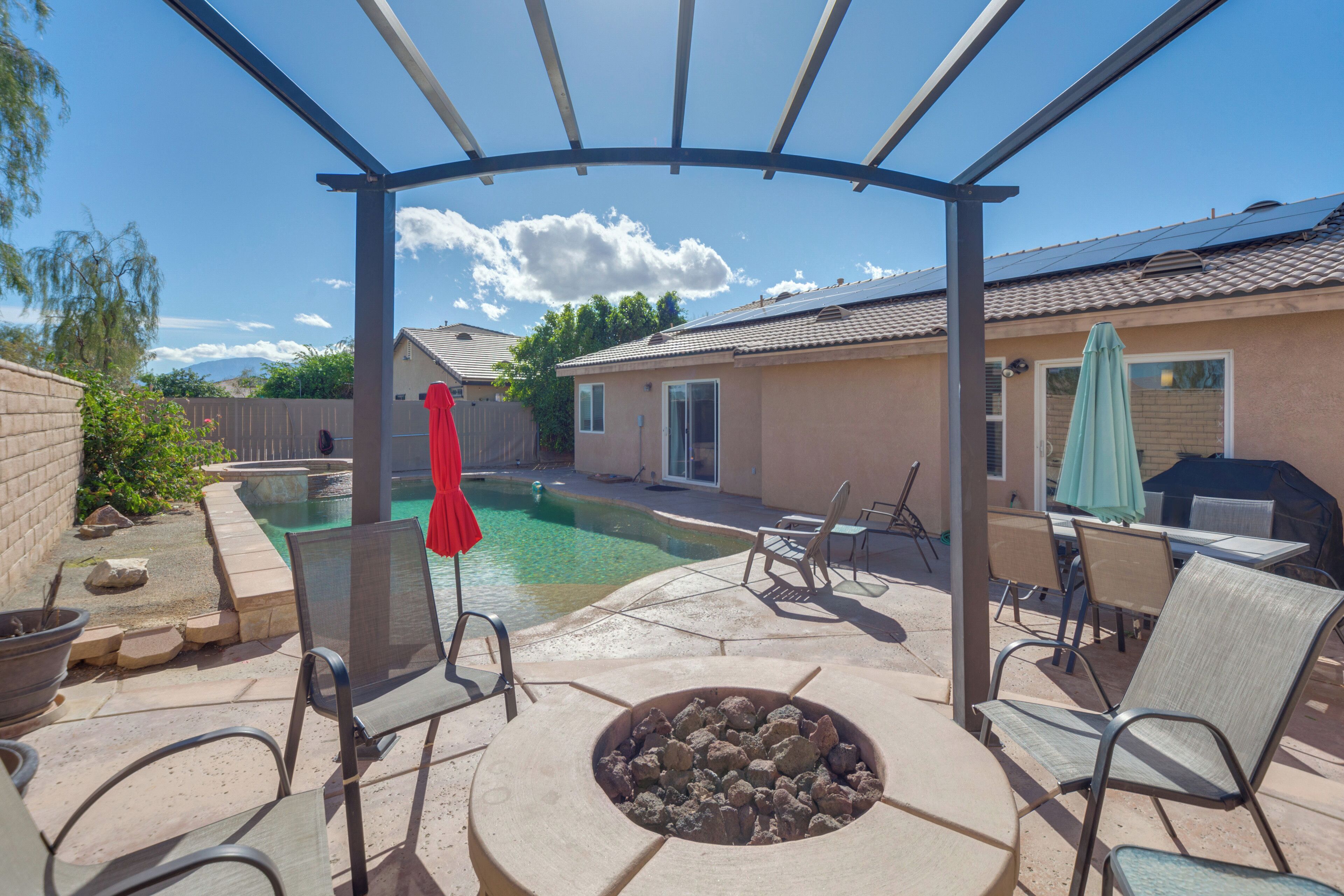 A backyard with a swimming pool, patio furniture, and a covered seating area.