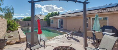 A backyard with a swimming pool, patio furniture, and a covered seating area.