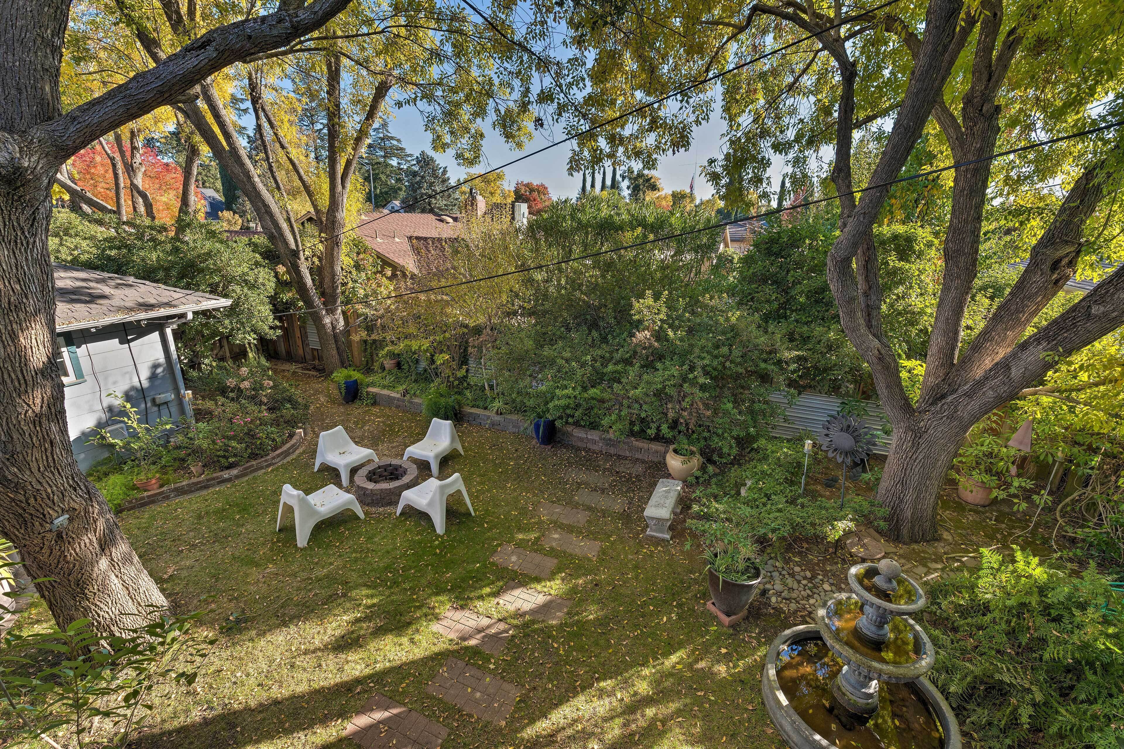 Un giardino sul retro con un braciere, sedie bianche e un vialetto in pietra.