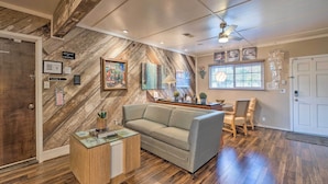 A modern living room with a herringbone wood wall, a sofa, a coffee table, and a dining area with a chair and table. - Luxurious Downtown Lodi Apartment in Wine Country! (Lodi)