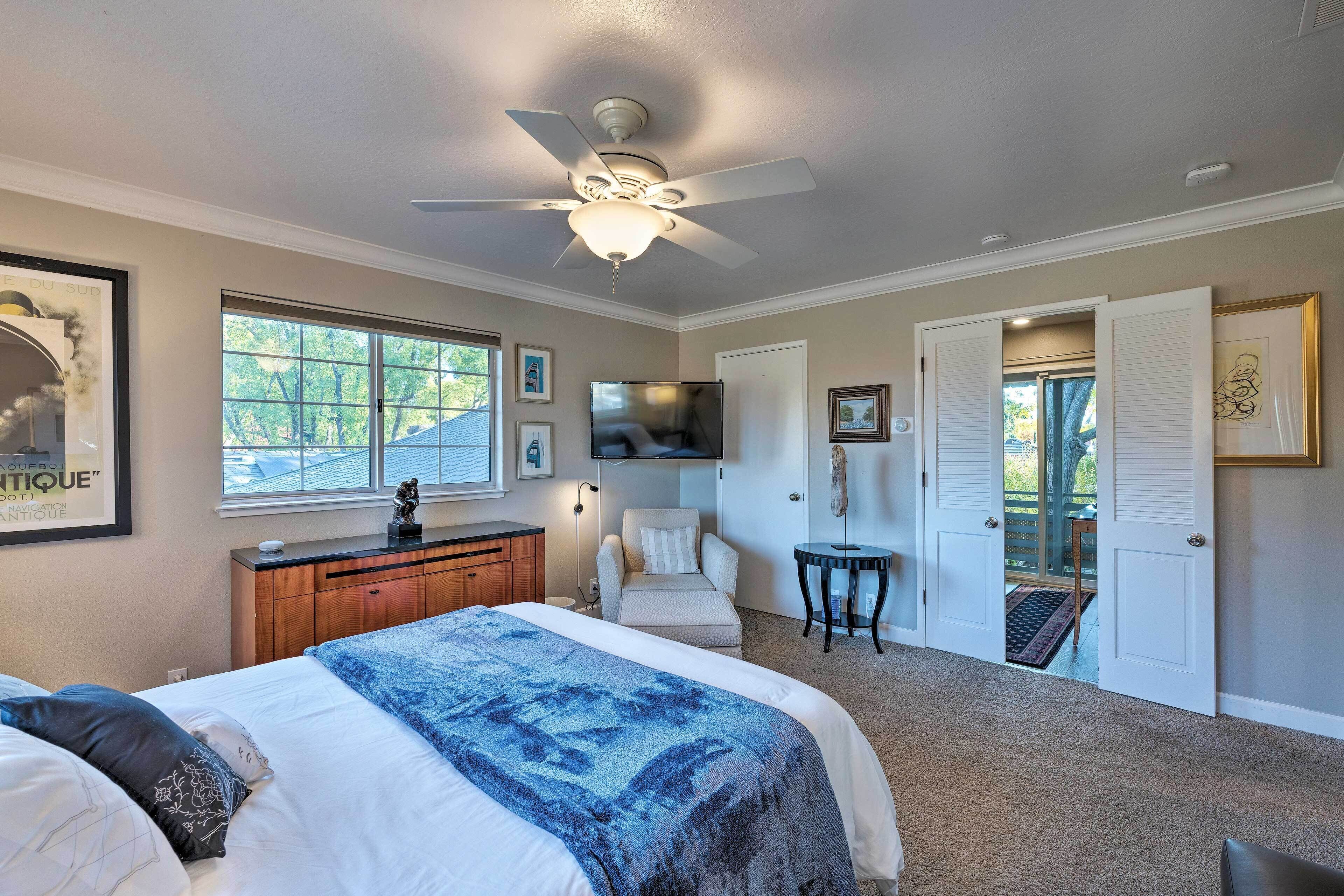 A bedroom with a bed, a ceiling fan, a dresser, a chair, a TV, and a door leading to a balcony.