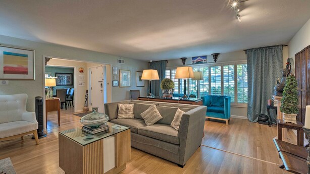 A spacious living room with a grey sofa, a glass coffee table, and a wooden side table. There is a blue armchair and a small table with a potted plant. - Spacious Wine Country Home: 1 Mi to Downtown Lodi! (Lodi)