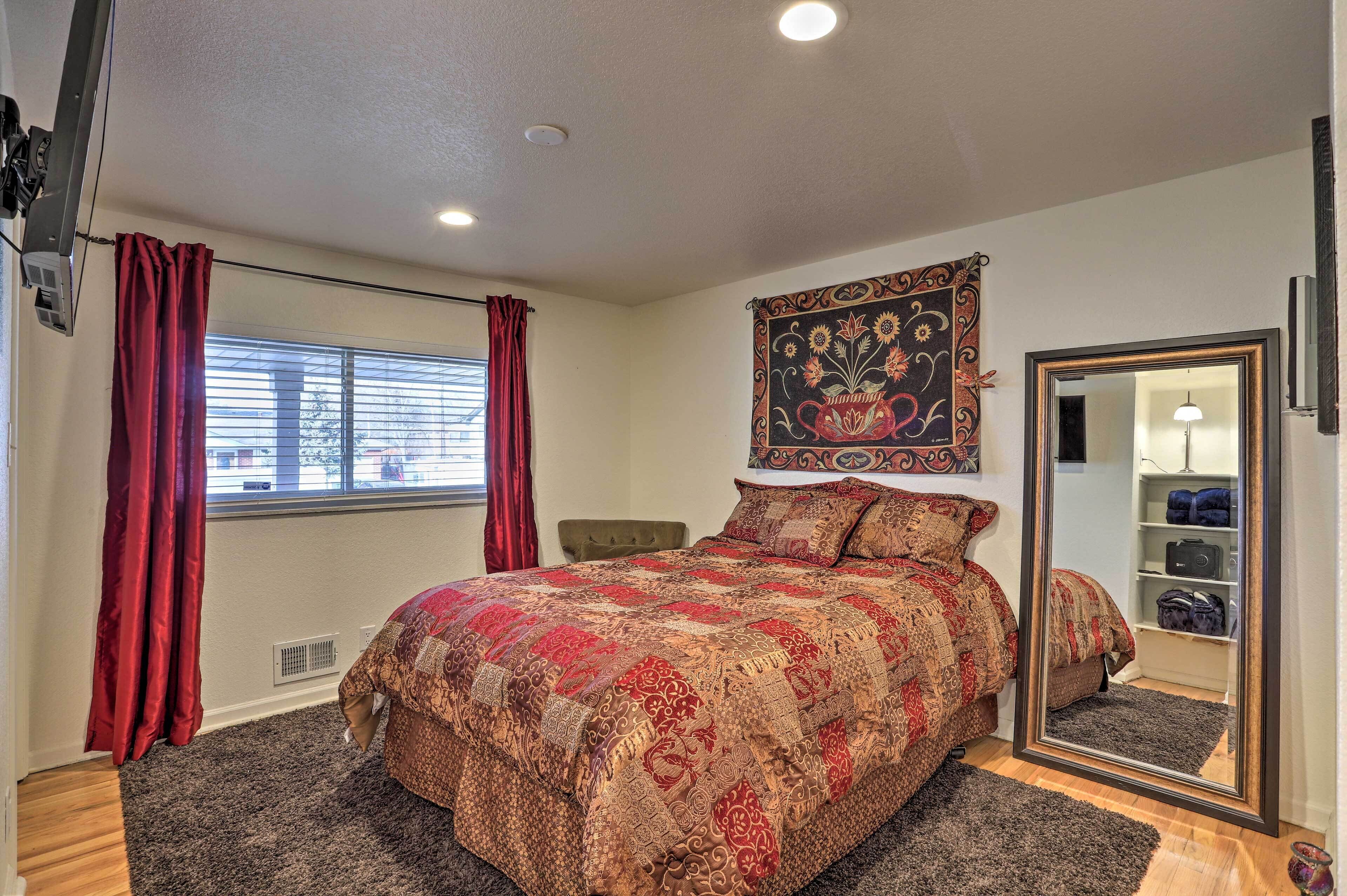 A bedroom with a large bed, a mirror, a window with curtains, and a tapestry on the wall.