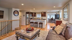 A spacious living room with a wooden staircase, a kitchen with a central island, and a dining area. - Private Yard + Patio: Denver Area Home! (Northglenn)