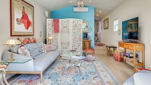A living room with a blue wall, a sofa, a glass coffee table, a TV on a wooden stand, and a patterned rug. - Romantic Casita w/ Garden + Deck 2 Miles to Plaza! (Sonoma)
