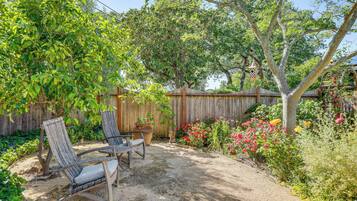 A backyard with a wooden fence, two chairs, a table, and various plants and flowers.