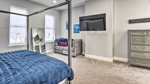 A bedroom with a four-poster bed, a gray sofa, a TV, and a dresser. - Baltimore Abode, Walk to Cross Street Market! (Baltimore)