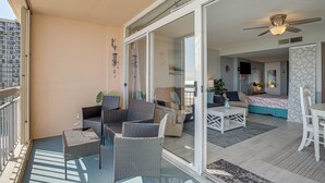 Ein Balkon mit Korbmöbeln, eine Schiebetür zu einem Wohnbereich mit Sofa, Couchtisch und Esstisch.