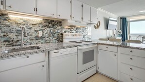 Eine moderne Küche mit weißen Schränken, einer Granit-Arbeitsplatte, einer Edelstahl-Spüle und einem eingebauten Backofen.