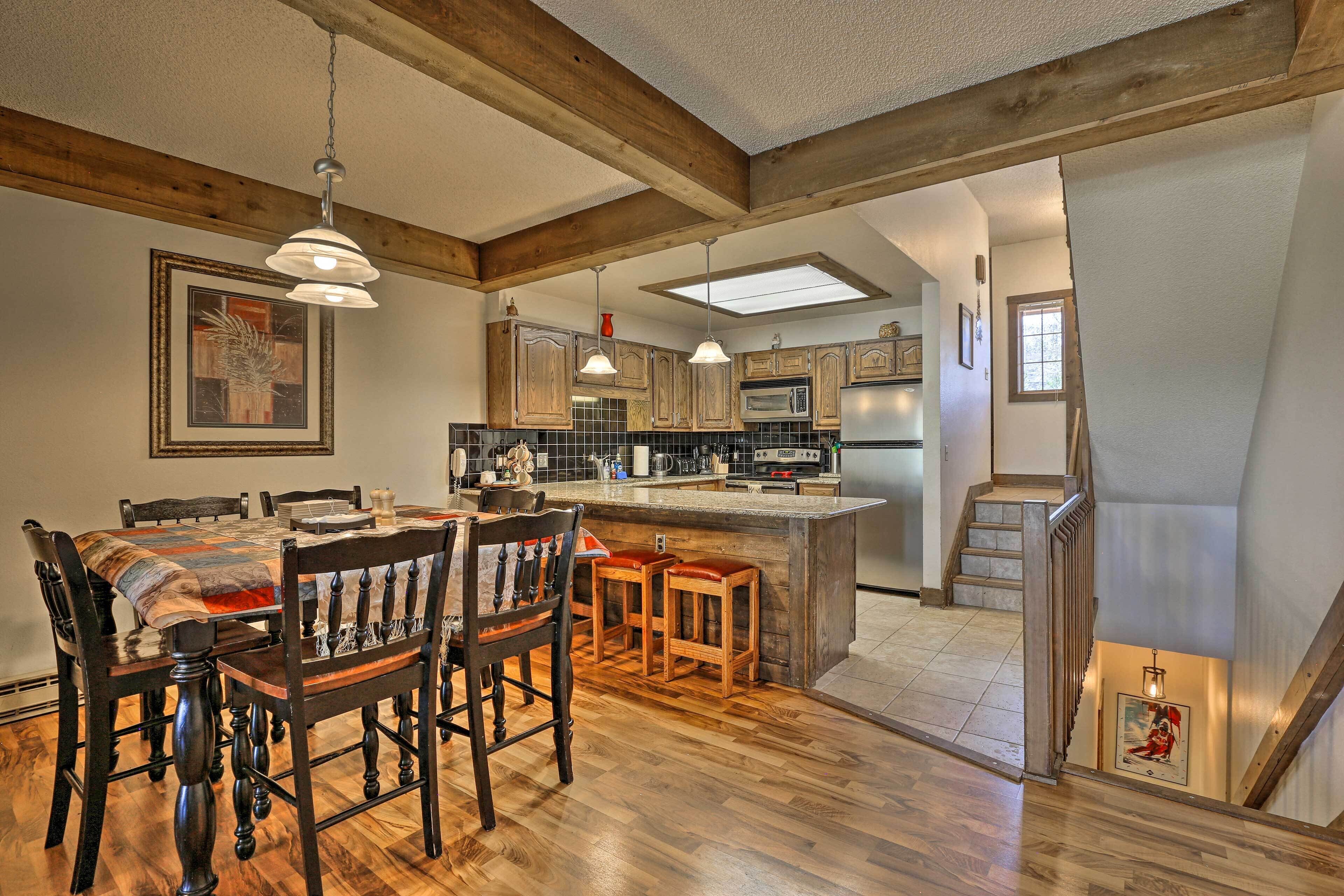 A spacious kitchen with wooden beams, a dining area with a large table and chairs, and a small island with stools.