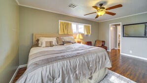 A bedroom with a large bed, a ceiling fan, a window with curtains, and a TV mounted on the wall. - Tulsa Home w/ Yard: 5 Mi to Downtown! (Tulsa)