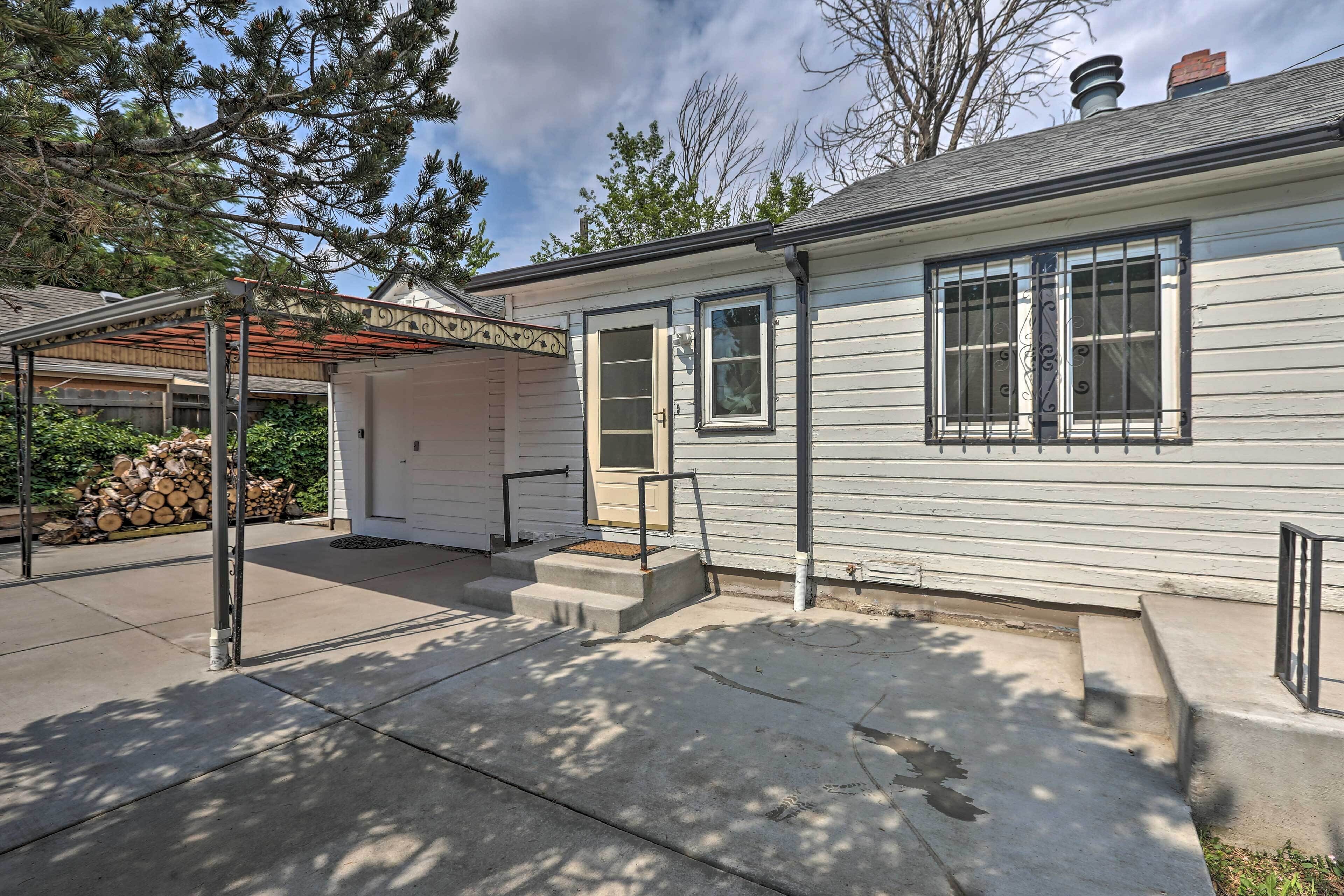 A single-story house with a covered patio, a front door, and a small front yard with a firewood stack.