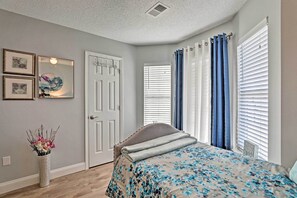 A bedroom with a bed, a door, a window with blinds, and a vase with flowers. - Beach-themed Retreat: 10 Mi to Downtown Charleston (North Charleston)