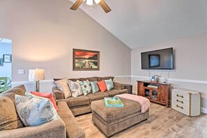 A living room with a brown sofa set, a television mounted on the wall, and a wooden cabinet with drawers. - Beach-themed Retreat: 10 Mi to Downtown Charleston (North Charleston)
