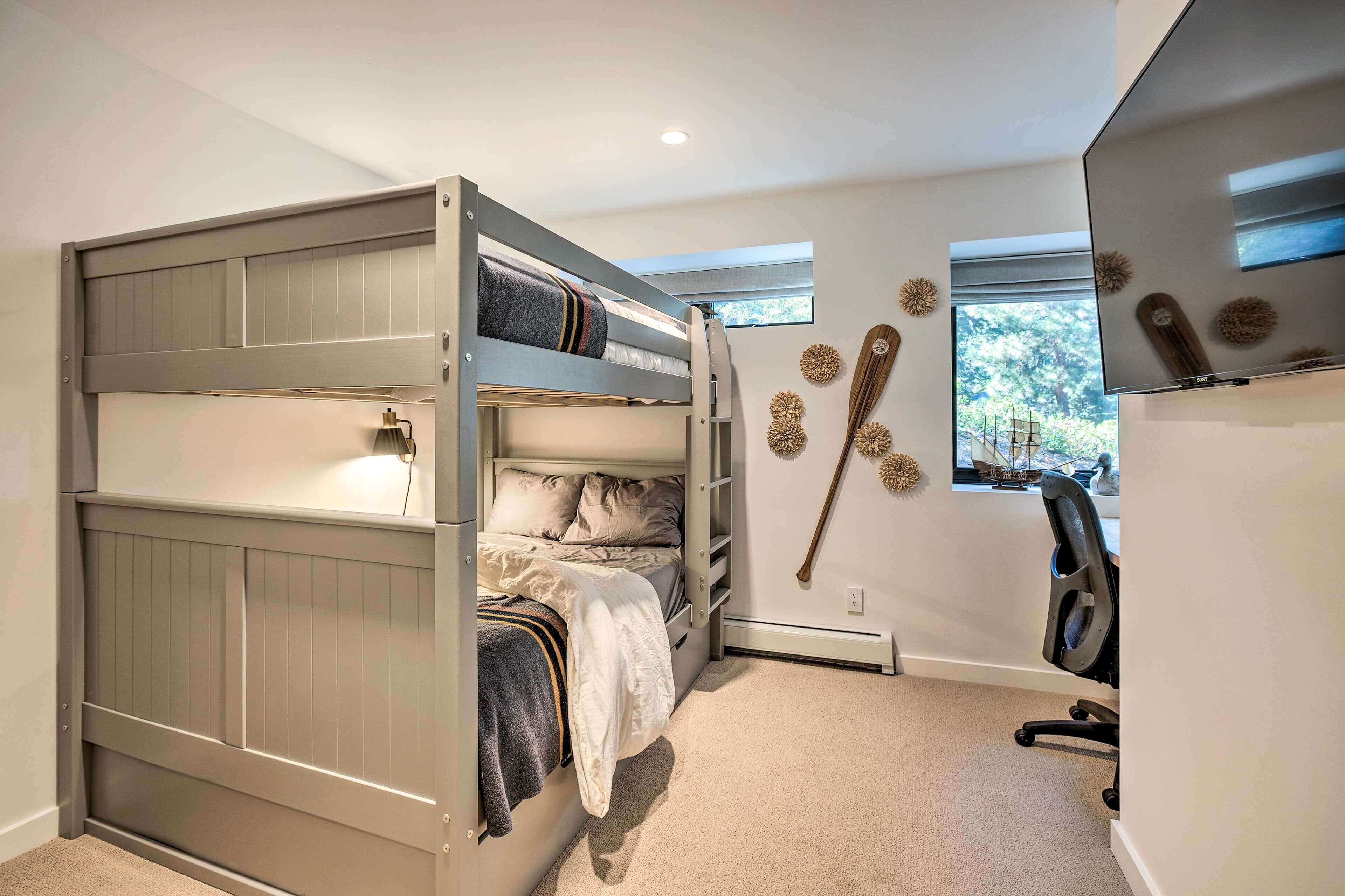 A bunk bed with a desk and chair, a window with a view of trees, and decorative wall art.