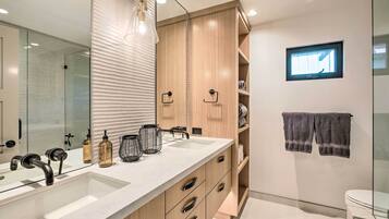 A modern bathroom with a large mirror, dual sinks, wooden cabinets, and a small window.