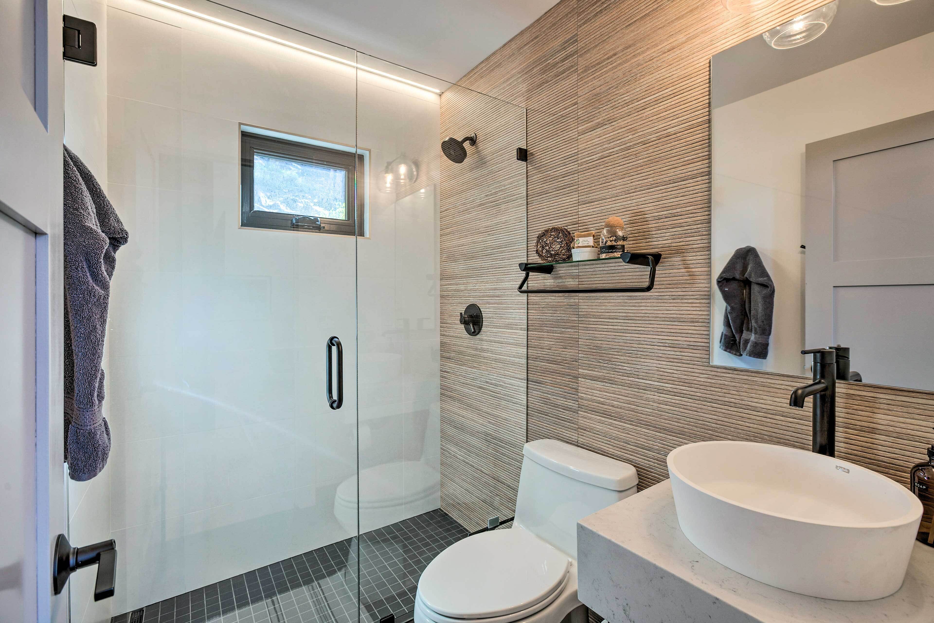 A modern bathroom with a glass-enclosed shower, a white toilet, and a large oval sink.