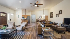 A spacious living room with a large sofa set, a coffee table, and a TV. There is a kitchen in the background with wooden cabinets and a refrigerator. - Cottonwoods 419 (Moab)